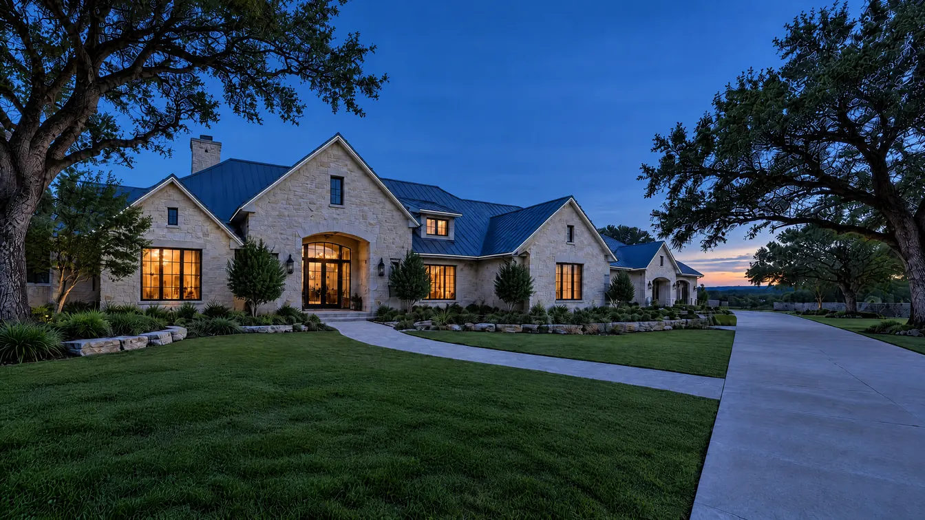 A limestone house at blue hour, its rooflines dark, the lights not yet on.