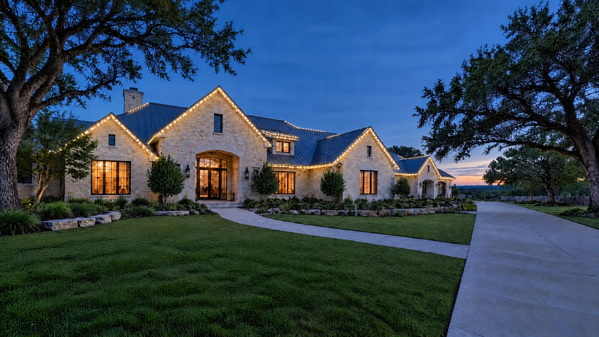 The same limestone house with a slim track of small warm white lights along every roofline.