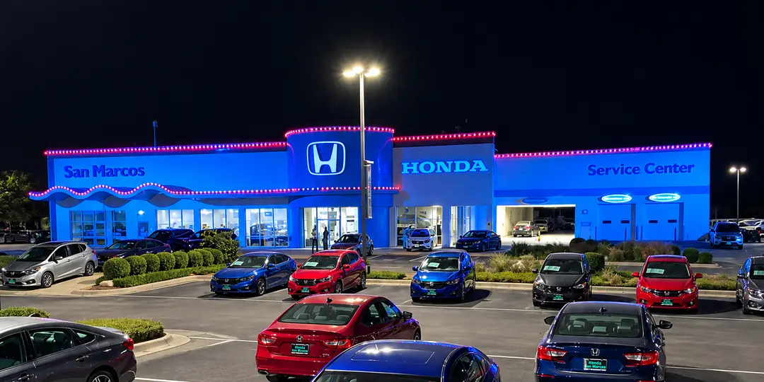 Honda San Marcos at night, a run of pink-red lights along every roofline of the dealership and its curved front canopy, with new cars parked in the lot.