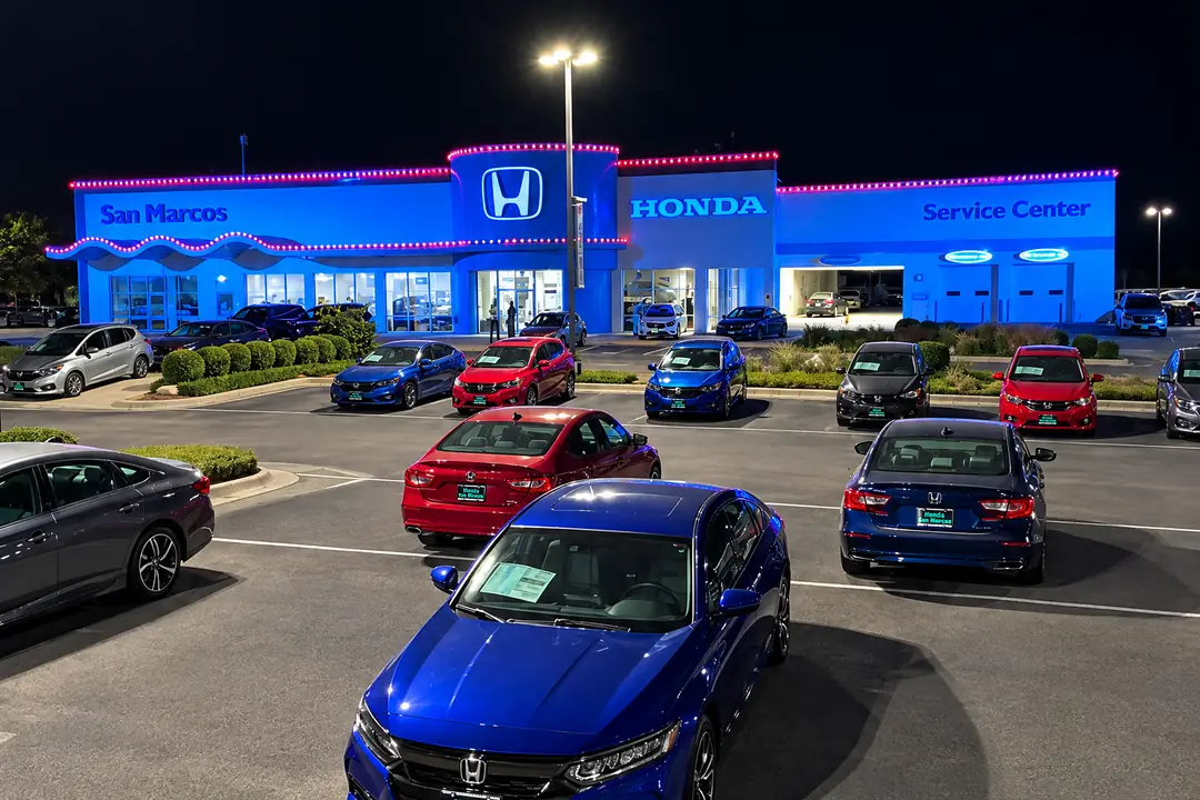 Honda San Marcos at night, a run of pink-red lights along every roofline of the dealership and its curved front canopy, with new cars parked in the lot.